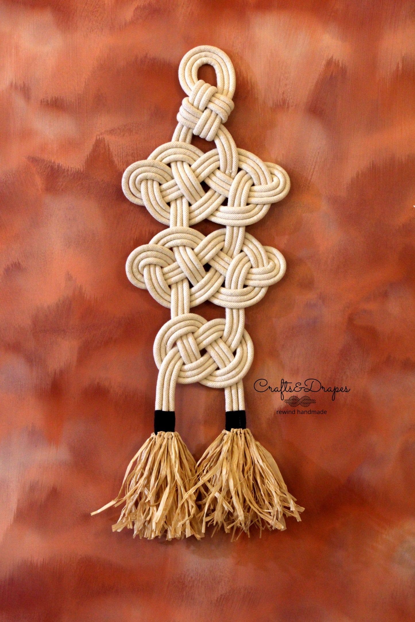 Celtic knot rope wall art with intricate design and raffia fringe, combining cultural heritage and natural textures to create a captivating and elegant decorative piece.